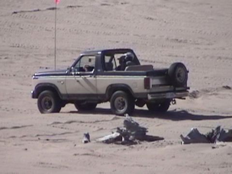 1995 Ford Bronco - Ford Bronco with removable top driving on sand dunes, spare tire mounted on rear.