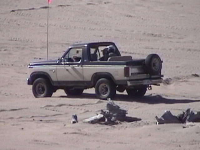 Ford Bronco with removable top driving on sand dunes, spare tire mounted on rear