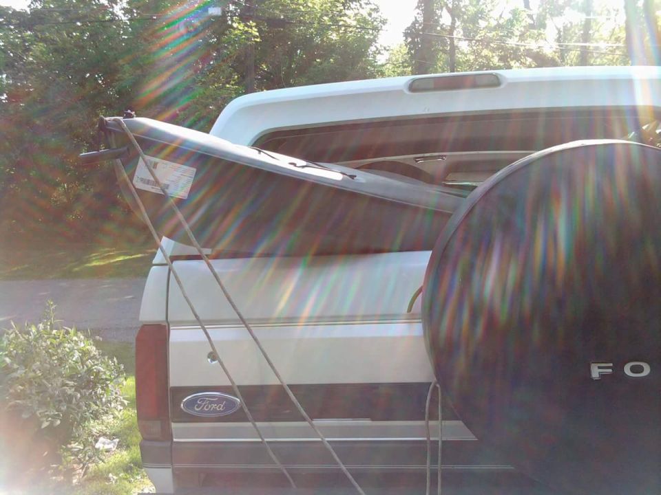 Ford pickup truck with a kayak strapped to the bed. Spare tire visible on the right