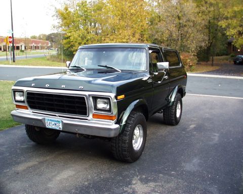 1995 Ford Bronco - A dark green (nearly black) full-size Ford Bronco SUV with a silver/two-tone lower body, chrome grille reading 'FORD', and chrome wheels, p…