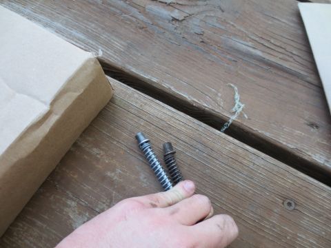1994 Ford F-350 - Two bolts with springs are held by a hand over a wooden deck, with a cardboard box to the left.