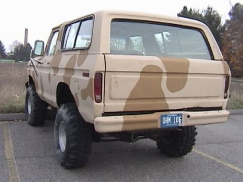 1995 Ford Bronco - Rear three-quarter view of a lifted late-1970s full-size Ford Bronco painted in tan and brown desert camouflage, with a removable hardtop,…
