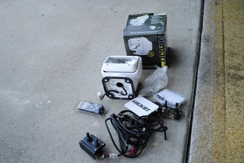 1986 Ford Bronco - A remote controlled spotlight, its box, and various accessories are laid out on a concrete surface.