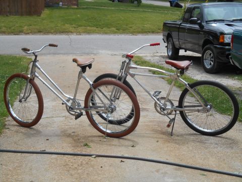 Two silver cruiser bicycles with brown seats and handlebars parked on a driveway. A black pickup truck is visi