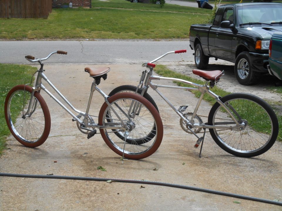 Two silver cruiser bicycles with brown seats and handlebars parked on a driveway. A black pickup truck is visible in the background