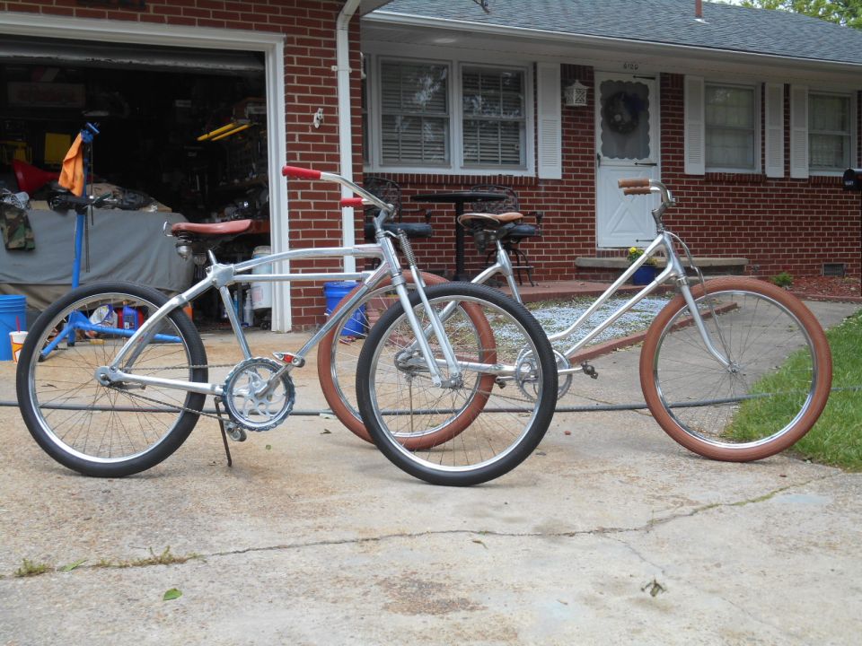 Two custom bicycles with chrome frames and brown tires parked in front of a brick house