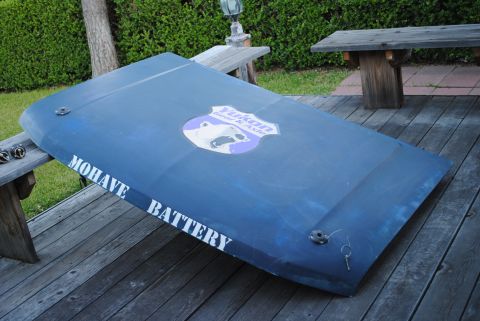 1986 Ford Bronco - A dark blue car hood, possibly from a 1986 Ford Bronco, rests on a wooden deck. The hood features white lettering that reads "MOHAVE BATTER…
