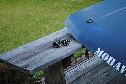 1986 Ford Bronco - Two black deck fittings with brass rings are placed on a weathered wooden picnic table next to a blue kayak or canoe. The kayak has the wor…