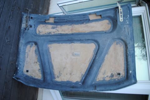 1986 Ford Bronco - The underside of a dark blue car hood is shown, with areas of exposed tan material and visible hinges. The hood is resting on a wooden surf…
