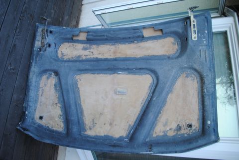 1986 Ford Bronco - The underside of an open car hood, possibly from a 1986 Ford Bronco, is shown resting on a wooden surface next to a window. The hood is dar…