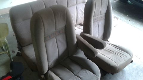 1996 Ford Bronco - Two tan fabric captain's chairs with armrests and a section of a matching bench seat are displayed indoors. A decorative band with a repeat…