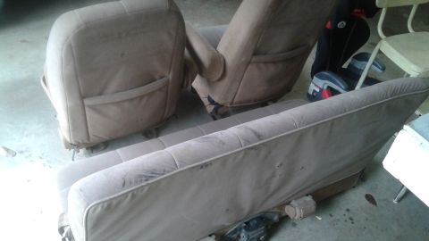 1996 Ford Bronco - Two tan cloth car seats and a matching bench seat are shown disassembled on a concrete floor. A black and gray child car seat is visible be…