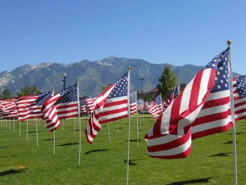 1979 Ford Bronco - Dozens of American flags are planted in a grassy field with mountains in the background under a clear blue sky.