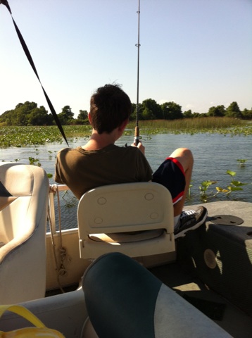 2007 Ford F-250 - A person fishes from the back of a boat on a sunny day. The boat has several seats and is surrounded by water with lily pads and trees in t…