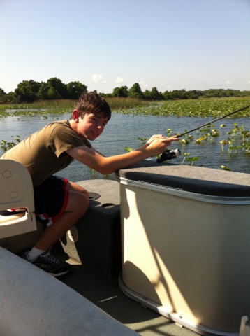 2007 Ford F-250 - A young boy is fishing from a boat on a lake with lily pads and trees in the background.