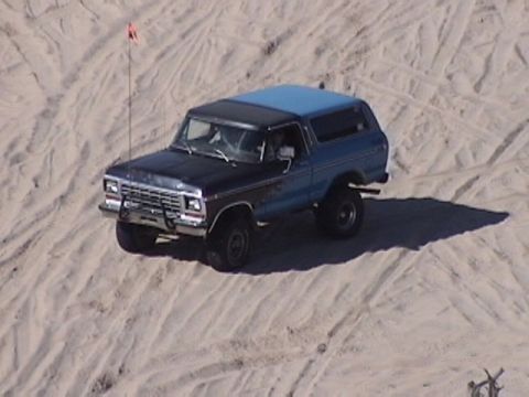 1995 Ford Bronco - Ford Bronco navigates sandy terrain, showing its distinctive grille and two-tone paint.