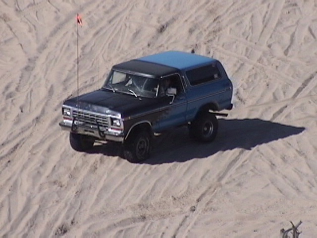 1978 Ford Bronco with blue top and black lower body driving on sand dunes