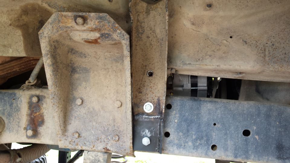 Close up of rusted vehicle undercarriage with modified bracket and bolts.