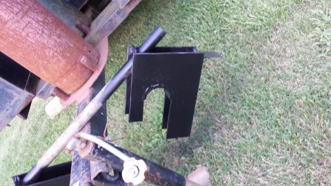 Black metal bracket with U-shaped cutout on rusty pipe, outdoors on grass.