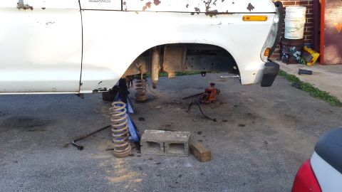 White 1970s Ford truck/SUV front passenger side, suspension disassembled, coil spring removed, jack and jack s