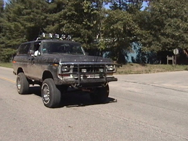 Dark 1978 Ford Bronco with bull bar and roof lights driving on a road