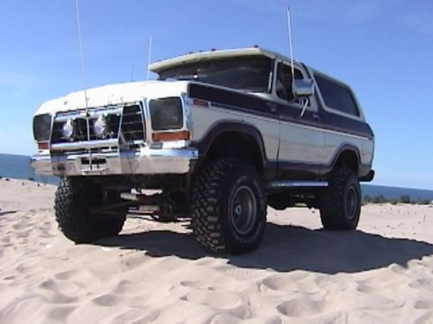 1995 Ford Bronco - This 1978 Ford Bronco, equipped with large off-road tires, is shown on a sandy terrain under a clear blue sky.