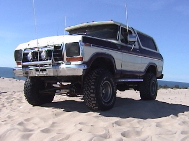 White and blue 1978 Ford Bronco with off-road tires parked on sand dunes