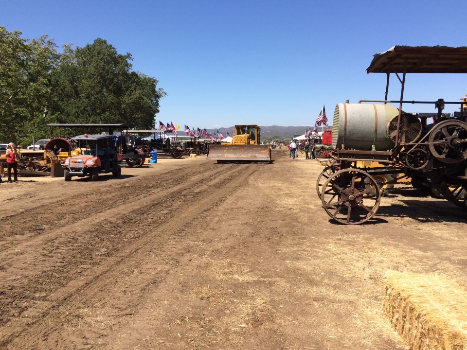 Old steam tractor and bulldozer on a dirt track with American flags.