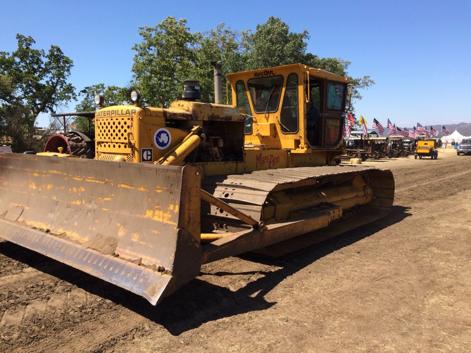 Yellow Caterpillar bulldozer with a large blade in the foreground, American flags and other machinery in the background.