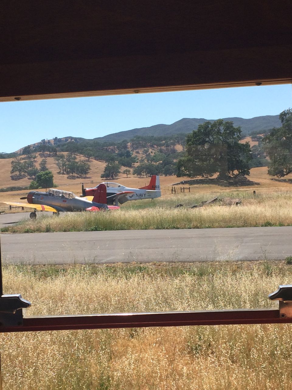 Two vintage airplanes on a runway with hills in the background.