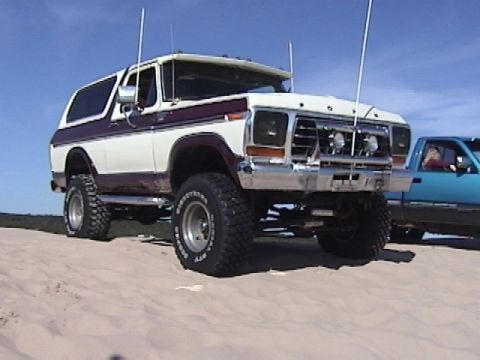 1995 Ford Bronco - This lifted 1978 Ford Bronco is parked on a sandy surface with a blue pickup truck nearby.