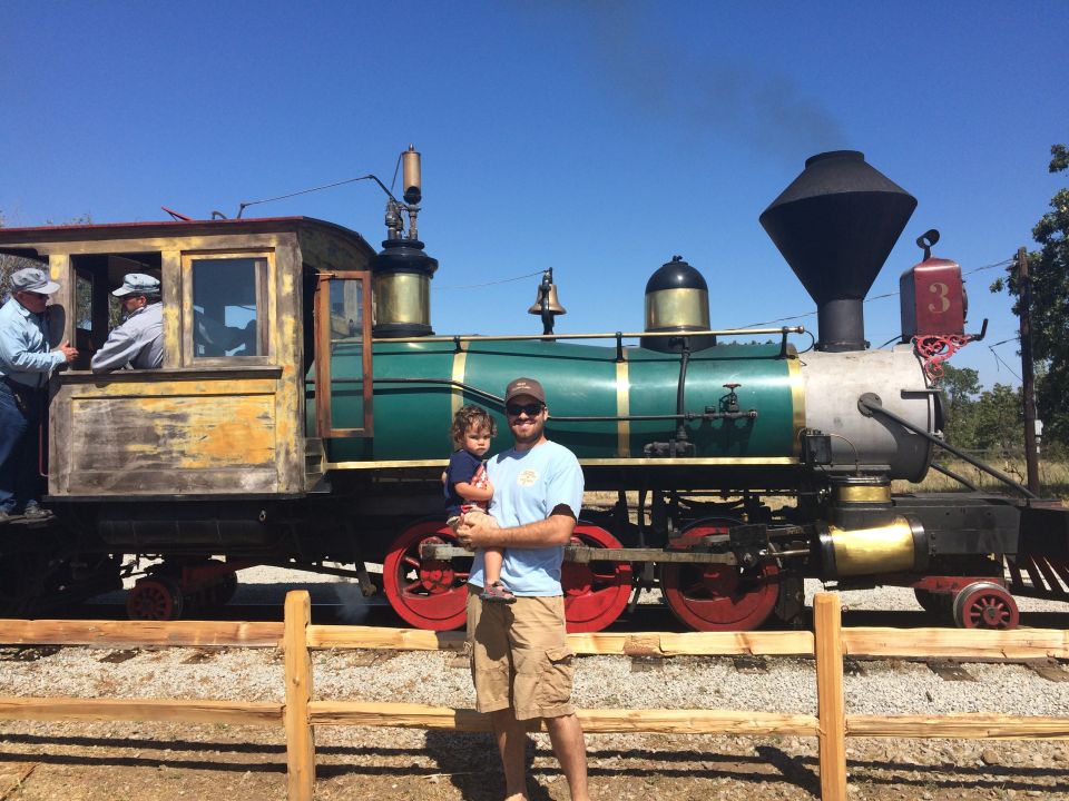 Man holding child in front of a vintage steam locomotive.