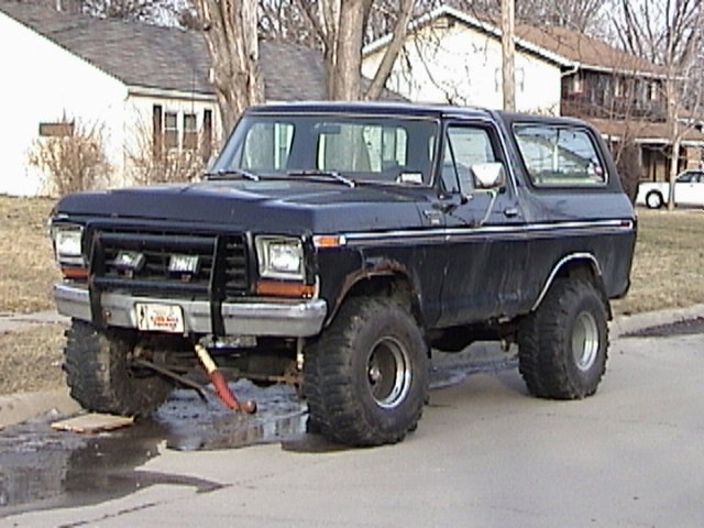 Dark blue Ford Bronco with a brush guard and large tires parked on a street