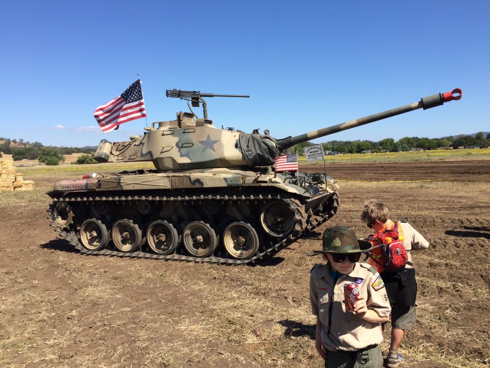 Camouflage tank with American flag, two scouts in foreground.