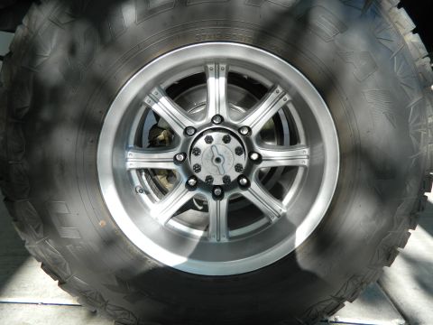 1979 Ford Bronco - A close-up, low-angle shot shows a large, rugged off-road tire mounted on a silver multi-spoke wheel. The tire has prominent tread blocks a…