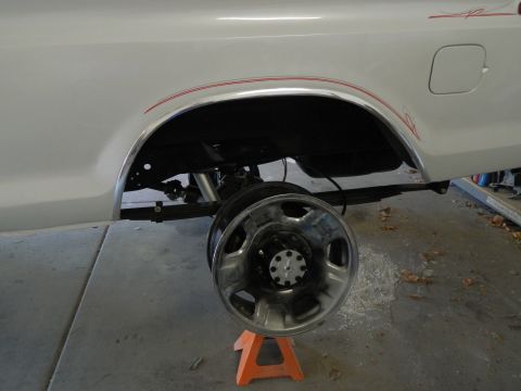 1979 Ford Bronco - The rear passenger side of a white Ford Bronco is shown with the wheel removed and resting on an orange jack stand. Chrome trim accents the…