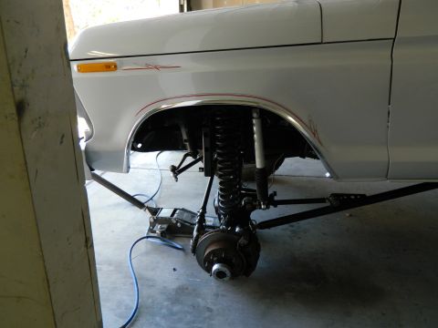 1979 Ford Bronco - A white Ford Bronco is shown from the side with the front wheel removed and the suspension components exposed. The vehicle is supported by…