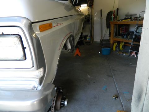 1979 Ford Bronco - A silver pickup truck is parked in a garage, with its front passenger side wheel removed and supported by an orange jack stand. Tools and s…