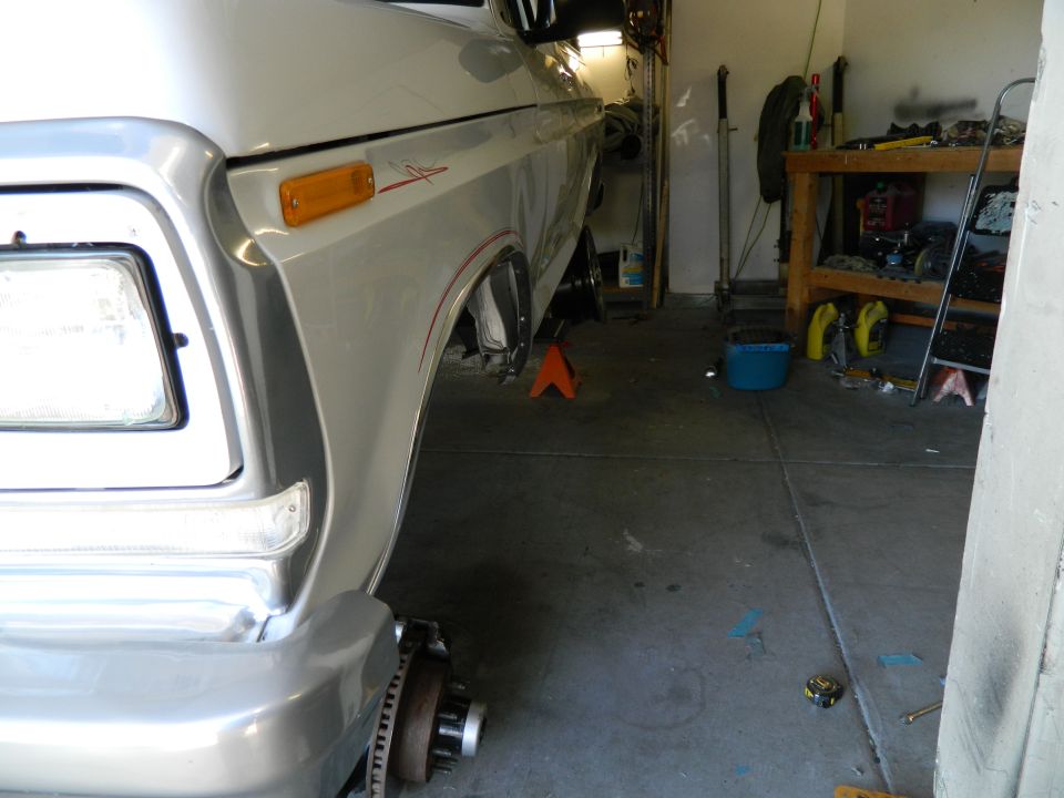 Silver pickup truck with front passenger wheel removed, supported by jack stand in garage.