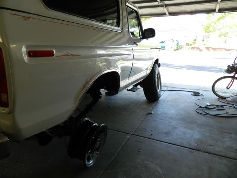 1979 Ford Bronco - The rear passenger side of a white Ford Bronco is shown in a garage with the rear wheel removed and resting on the ground. A bicycle is vis…
