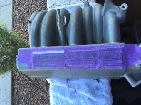 1996 Ford Bronco - A close-up, angled shot shows a gray metal intake manifold, possibly from a 1996 Ford Bronco, with purple masking tape applied to its surfa…