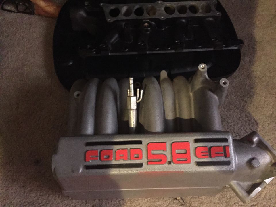Silver Ford 5.8 EFI intake manifold with red lettering on carpet