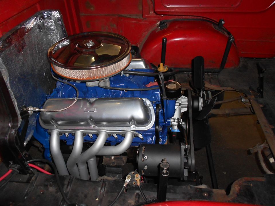 Close-up of a V8 engine with blue block, chrome air cleaner, and silver exhaust manifolds.