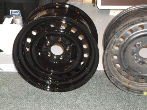 1999 Mercury Grand Marquis - Two steel wheels are shown, one is freshly painted black and the other is weathered and rusty. The black wheel is in the foreground, angled…