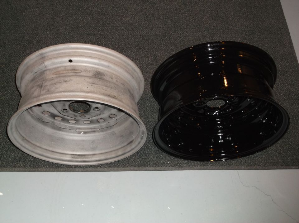 Two car rims, one unpainted and one glossy black, on a carpeted surface.