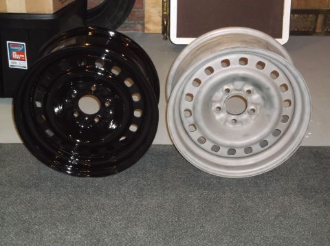 1999 Mercury Grand Marquis - Two car wheels are shown side-by-side on a carpeted floor. The wheel on the left is glossy black, and the wheel on the right is a matte sil…