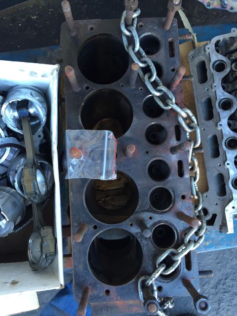 1946 Jeep Willys - A close-up view of a disassembled engine block with pistons and connecting rods in a white box to the left. A metal chain is draped across…