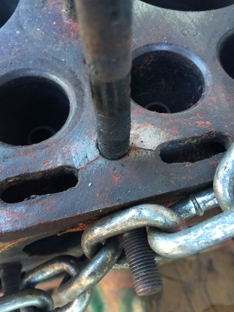 1946 Jeep Willys - Close-up view of a rusty metal engine component with a threaded bolt and a metal chain attached.