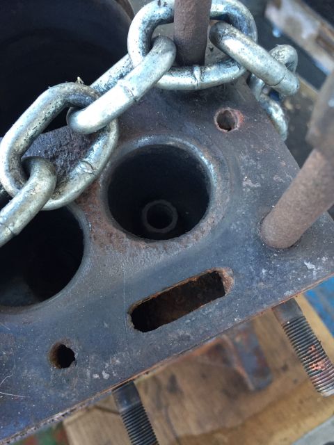 1946 Jeep Willys - A close-up, high-angle shot of a rusty metal engine part with a chain draped over it. Visible are several holes and a rectangular cutout, s…