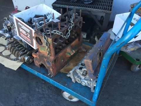 1946 Jeep Willys - A collection of engine parts, including a rusty engine block, a crankshaft, pistons, and a cylinder head, are arranged on a blue cart. A bo…